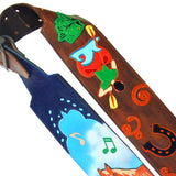 A close-up of a handcrafted custom guitar strap made from brown leather, decorated with colorful hand-painted and Kidskin appliqué motifs including a Bass fish, a Kayak, and black and orange decorative elements.