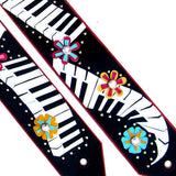 A black guitar strap featuring a Kidskin piano keyboard and flower overlays.  Centered with Swarovski Crystals.  Designer guitar strap owned by Kristin Chenoweth.